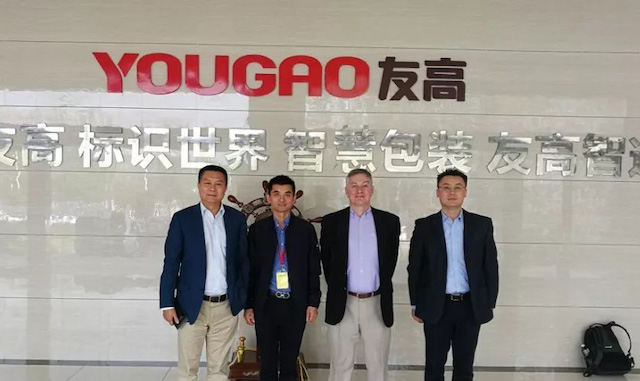 四名男子在YOUGAO友高墙面标志前合影