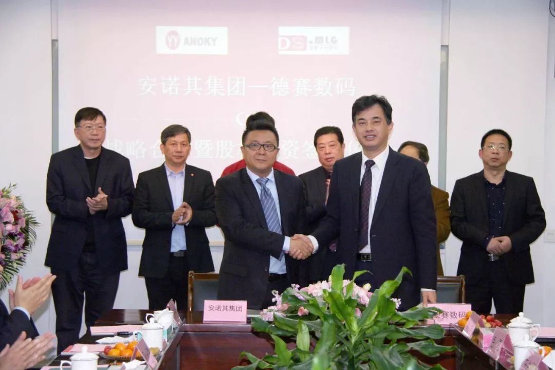 会议室中两名男子握手，布景显示安诺其集团与德赛数码文字