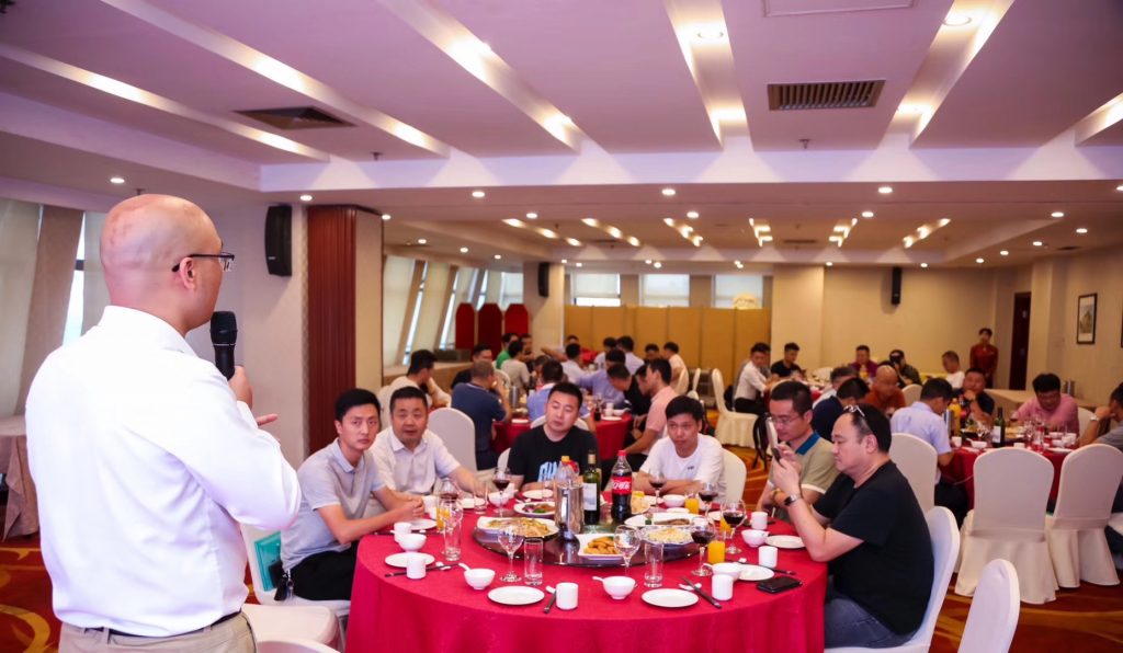 男子手持发话器，宴会厅人员围坐圆桌
