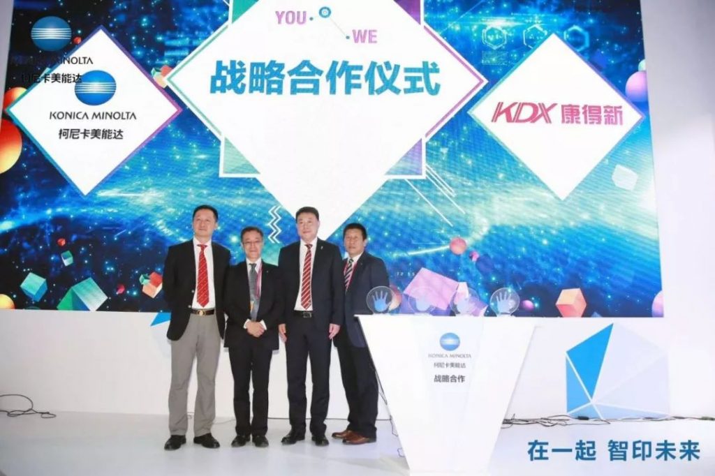 四名男子在柯尼卡美能达与KDX康得新标志布景前合影