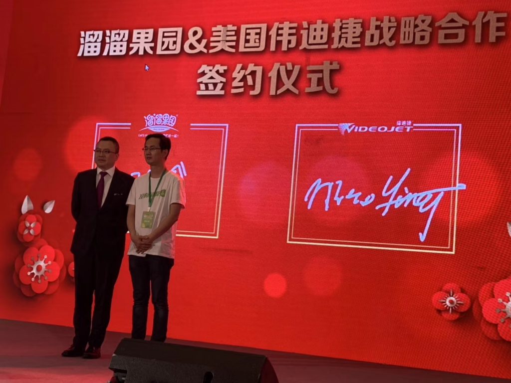 两人在溜溜果园与伟迪捷战术合作签约典礼布景前合影