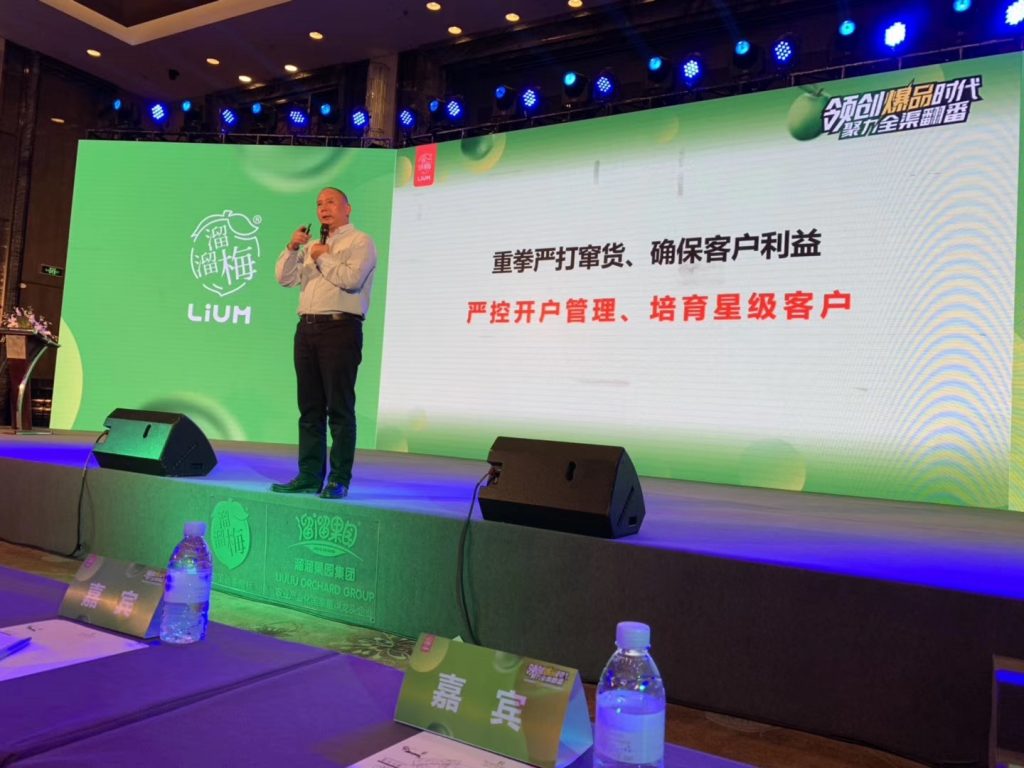 男子持发话器站在含渠路治理文字的绿色舞台屏幕前
