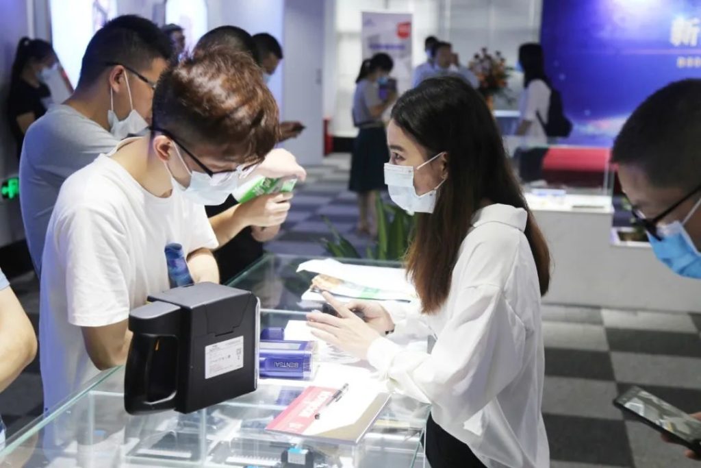 戴口罩的人员在展示柜旁互换，柜上放有玄色设备