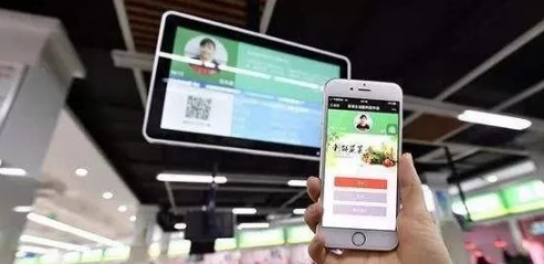 手持手机的绿色页面与卖场上方带二维码的显示屏