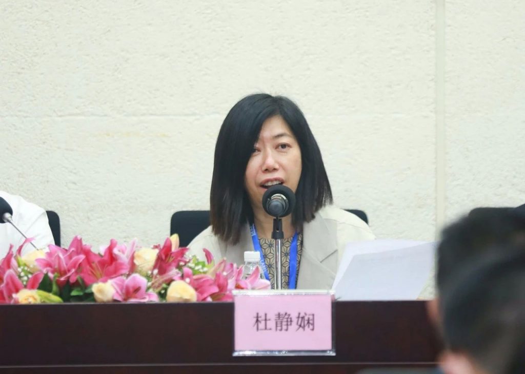 会议桌前的女子、麦克风、花束与杜静娴桌牌